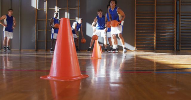 Diverse male basketball team wearing blue sportswear practice dribbling ball. basketball, sports training at an indoor court.