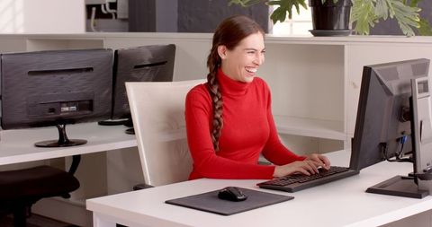 Smiling Woman at Office Desk Typing on Computer