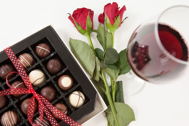 Bunch of roses, champagne bottle, wine glass and assorted chocolate box against white background
