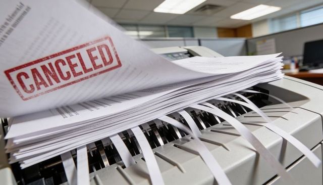 Shredding canceled contracts and documents in office shredder with red canceled stamp