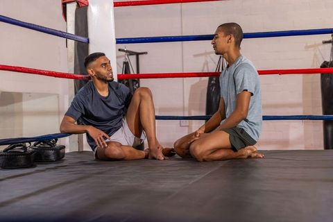 Asian male boxers resting and talking in boxing ring showing post-training camaraderie
