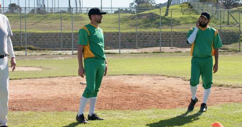 Baseball Teammates Standing on Sunlit Infield in Green and Yellow Uniforms During Practice