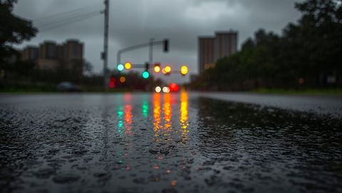 Neon traffic light reflections on wet asphalt at rainy urban intersection, low-angle bokeh