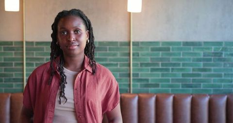 Confident black woman standing in cozy cafe with green tile wall and leather banquette
