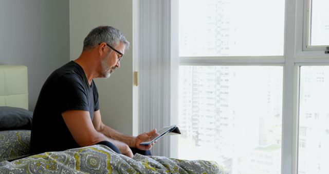 Middle-aged Man Reading Tablet by Window in Bedroom - Download Free Stock Images Pikwizard.com