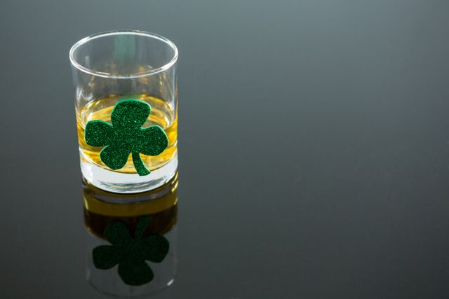 Glass of whiskey decorated with a green shamrock, perfect for St. Patrick's Day celebrations. Ideal for use in holiday promotions, festive advertisements, Irish-themed events, and social media posts highlighting traditional Irish culture and festivities.