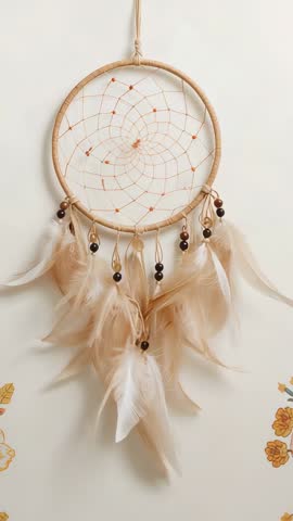 Vertical video of swaying dreamcatcher with feathers and beads on bedroom wall, boho decor