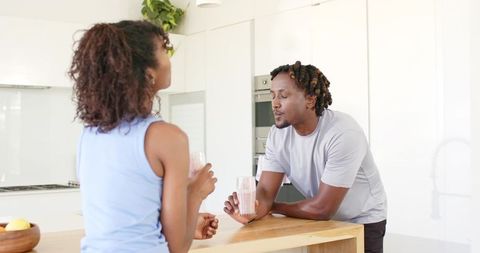 African American couple chatting over smoothies at modern bright kitchen island
