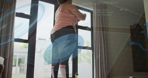 Plus-size woman pausing workout checking smartwatch by patio doors with holographic HUD