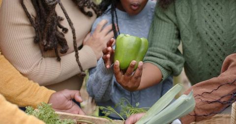 Multigenerational family reaching for green bell pepper in woven basket at farmers market
