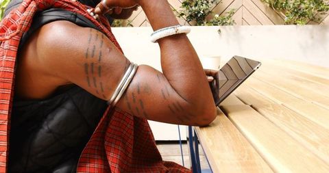 Tattooed arms leaning on wooden table with tablet and coffee cup, relaxed alfresco lifestyle