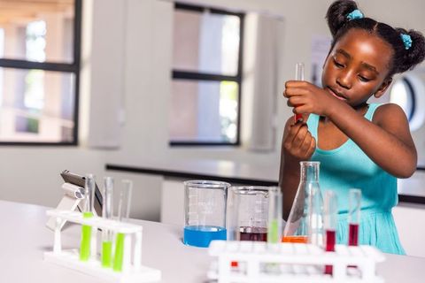 African american girl conducting colorful chemistry experiment with test tubes and tablet