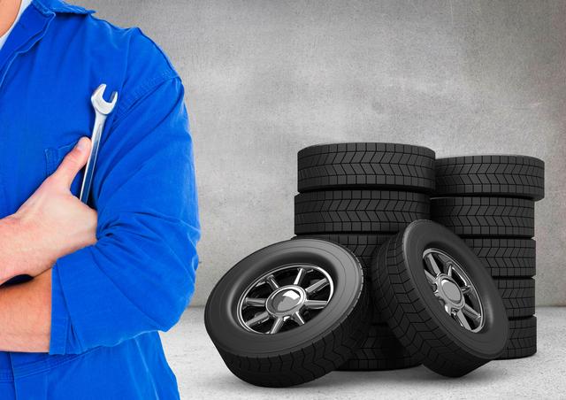 Mechanic in blue uniform holding a lug wrench with stacks of tires in the background. Ideal for use in automotive repair advertisements, maintenance service promotions, and workshop-related content.