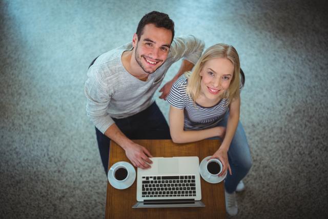 Portrait of smiling couple using laptop while having black coffee in cafÃ©