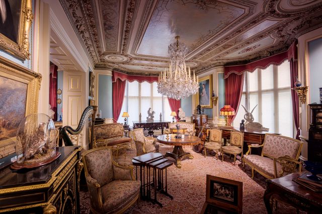 This image showcases a luxurious vintage living room featuring a grand chandelier, antique furniture, and richly ornamented ceiling. Perfect for use in articles or projects about historical home design, opulent interiors, antique collections, or Victorian style interiors. Ideal for interior design inspiration and architectural history blogs.