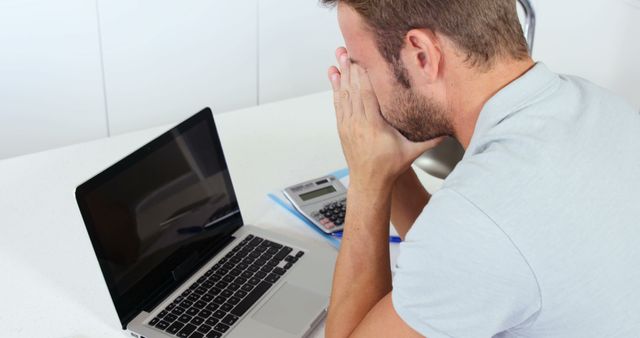 Upset man doing his accounting with a laptop in the kitchen