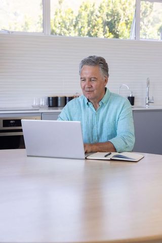 Mature man working on laptop at modern kitchen table in daylight