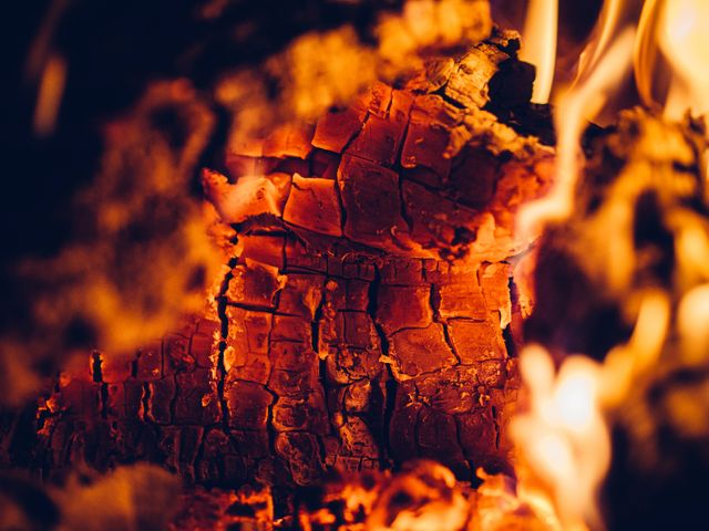 Close-up view of burning wood embers glowing in a fireplace, showing rich textures and warm colors. Ideal image for use in articles or blog posts about winter warmth, cozy home settings, fireplaces, survival tips, or home heating solutions. Can also serve as artistic background or design inspiration displaying fiery and glowing aesthetics.
