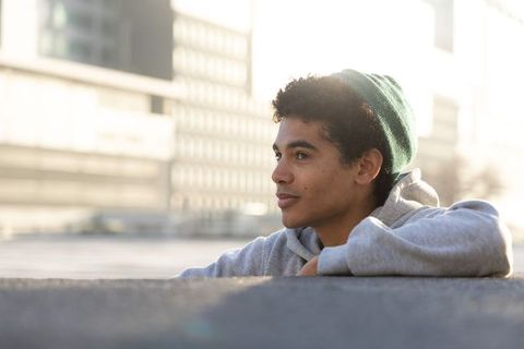 African american teen leaning on rooftop ledge wearing green beanie at golden hour