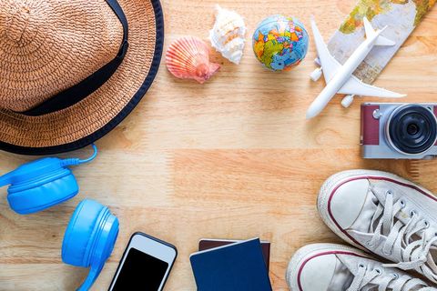Summer travel essentials flatlay wood table straw hat blue headphones camera passport