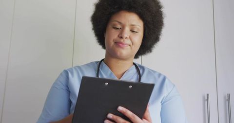 Nurse reviewing patient notes holding clipboard in light blue scrubs with stethoscope
