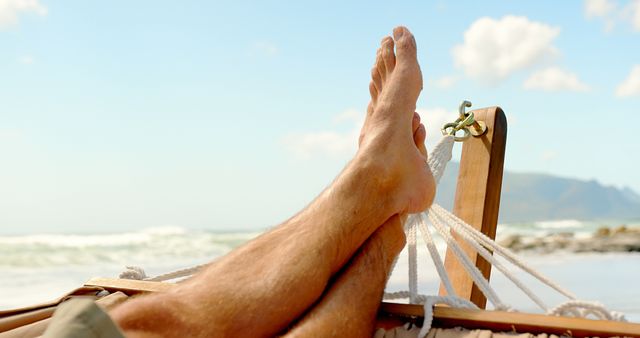 Close up of feet of caucasian man lying in hammock on beach. Summer, relaxation, leisure, vacation and lifestyle.