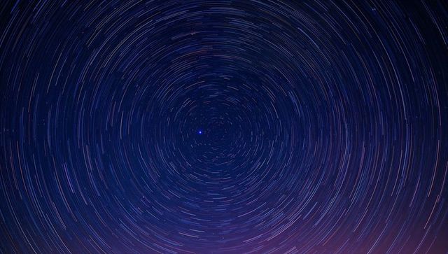 Concentric star trails circling north star over purple horizon long exposure night sky