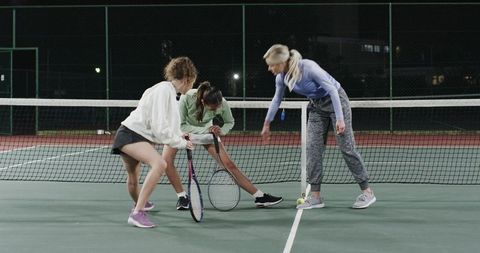 Women tennis team training at net under floodlights coach guiding players during night practice