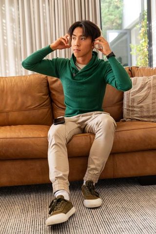 Asian man adjusting wireless headphones on leather sofa in cozy modern living room
