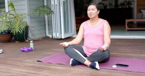 Meditating middle-aged asian woman practicing outdoor mindfulness on wooden deck patio