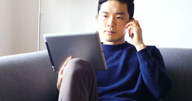 Focused Young Man on Tablet While Talking on Phone Sitting on Couch - Download Free Stock Images Pikwizard.com