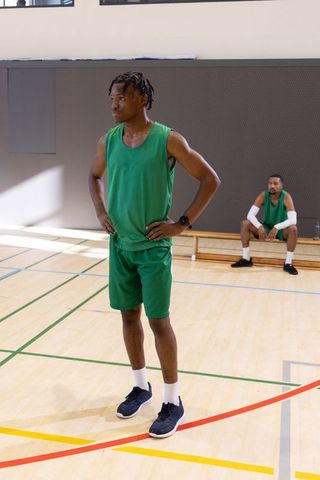 African american basketball player standing hands on hips in green jersey on court