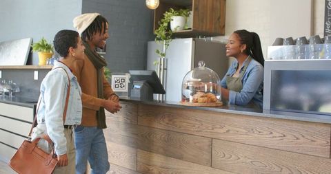 Young couple ordering coffee at cozy wood counter with friendly barista and pastries