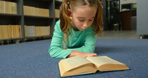 Young schoolgirl reading book on library floor