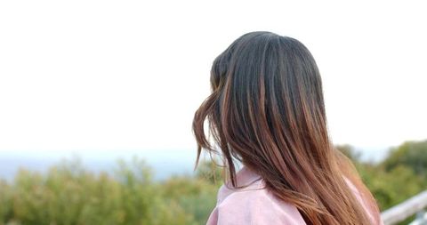 Woman gazing at coastal horizon from overlook wearing pink jacket back view serene