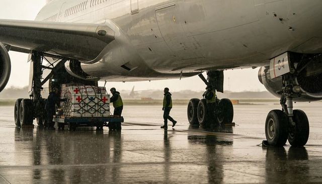Ground crew loading humanitarian aid pallet under heavy rain at cargo plane on wet apron