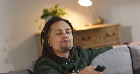Reclining man holding tv remote on couch in cozy living room with warm lighting