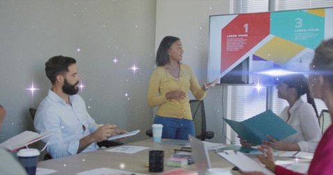 Woman presenting colorful slides while team collaborating around table with laptops