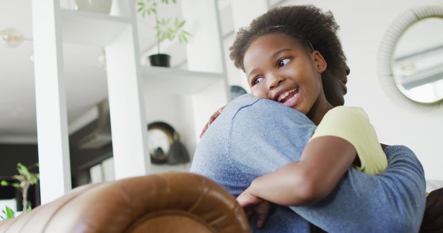 Father embracing his daughter in living room. Perfect for themes like family bonding, parent-child relationship, love, happiness, and affection. Useful for articles, blogs, brochures, and any content focusing on parenting, family dynamics, and emotional well-being.