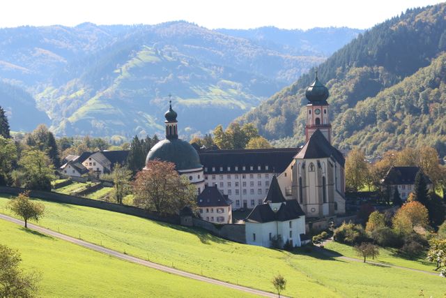 This image showcases a scenic view of a historic monastery nestled in the green hills of the Black Forest, Germany. Surrounded by vibrant autumn colors and mountainous landscape, this is perfect for travel blogs, tourism promotions, nature documentaries, and cultural heritage content.