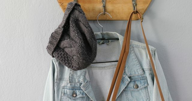 Casual denim jacket and knit hat hanging on wooden coat rack in home hallway. This image is perfect for illustrating home decor ideas, storage solutions, and showcasing casual fashion accessories. Ideal for use in lifestyle blogs, fashion websites, and interior design inspiration.