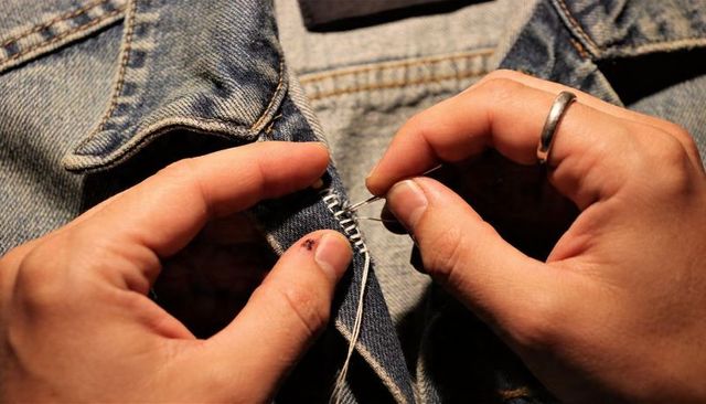 Closeup Hands Mending Denim Jacket Seam with Needle and White Thread, Textile Repair