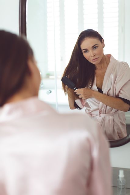 Reflection of woman in mirror combing hair in bathroom at home