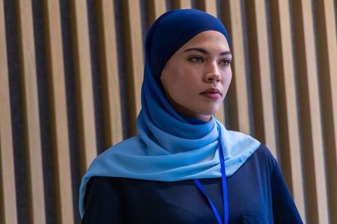 African professional standing in lobby wearing layered blue hijab conference headshot