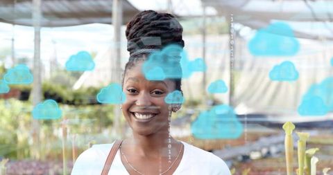 Smiling woman standing in greenhouse wearing white top with cloud computing overlay