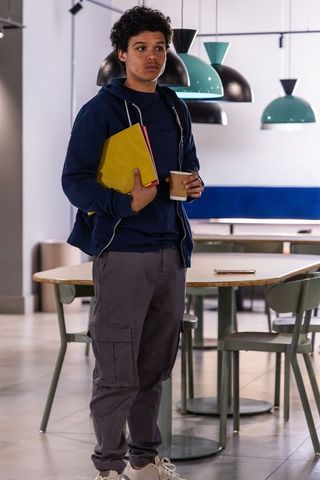 African american teenager standing in modern campus lounge holding notebook and coffee