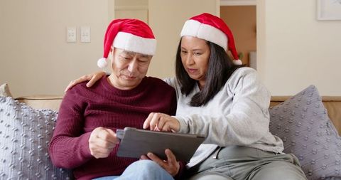 Senior couple in santa hats using tablet at home