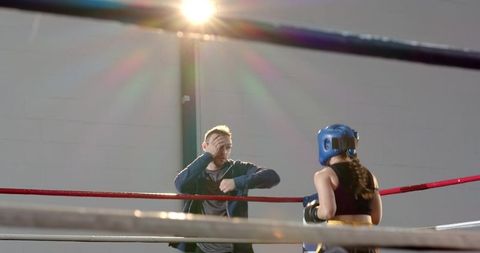 Trainer coaching female boxer in ring wearing blue headgear during sparring session