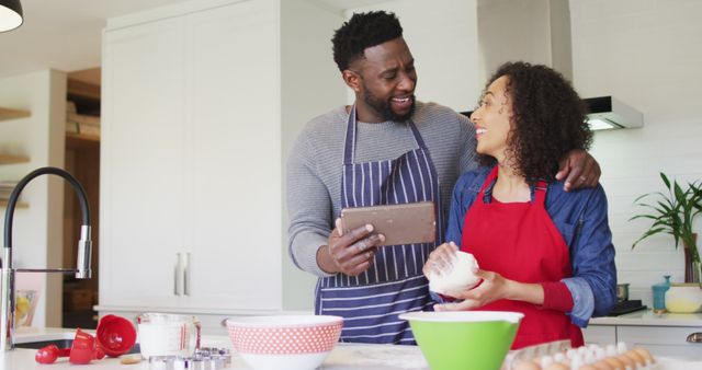 Happy african american couple wearing aprons, using tablet and baking together. family time, having fun together at home.