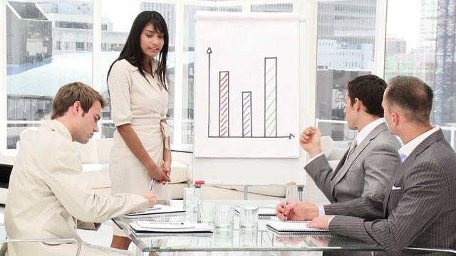 Group of business professionals discussing presentation of bar chart in modern conference room. Could be used for concepts like teamwork, collaboration, business strategy, corporate environment, and office settings.